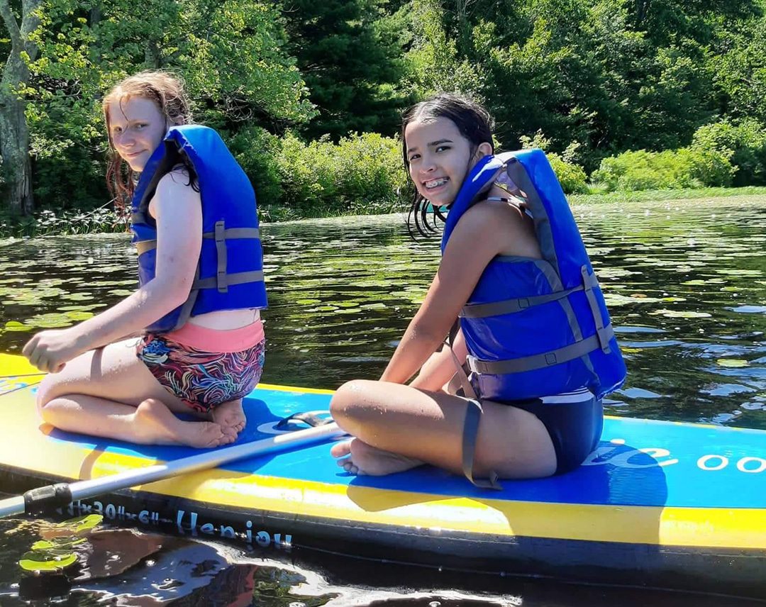 Two girls in blue life jackets on paddleboard