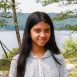 Smiling girl standing by lake in hoodie