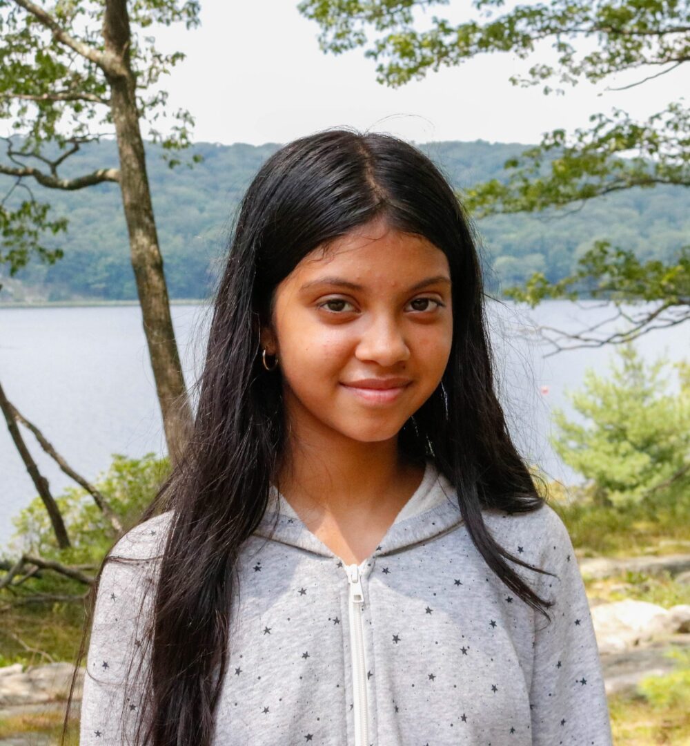 Smiling girl standing by lake in hoodie