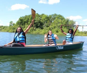 Three people canoeing on lake, raising paddles
