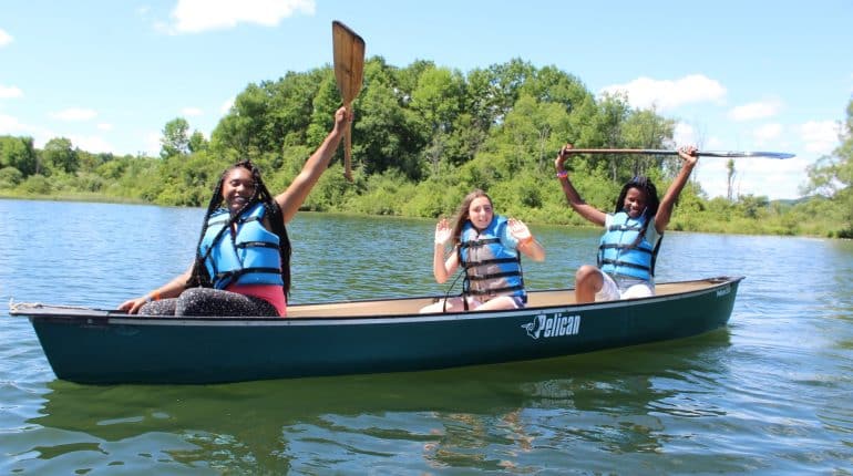 Three people canoeing on lake, raising paddles
