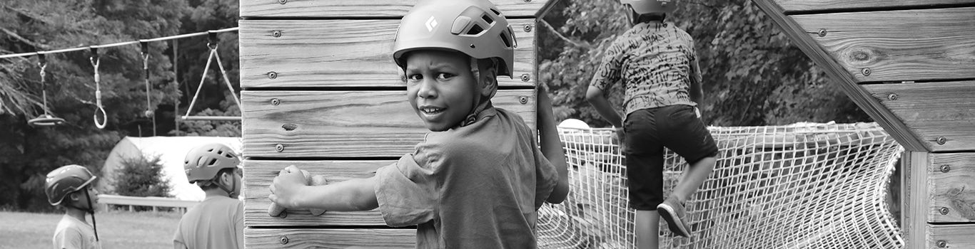 Children wearing helmets climbing wooden play structure