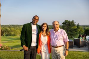 Three smiling adults posing outdoors by golf course
