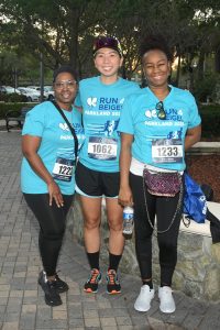 Three smiling runners wearing teal race shirts