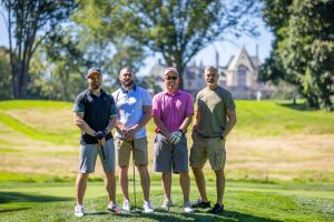 Four golfers posing with clubs on course