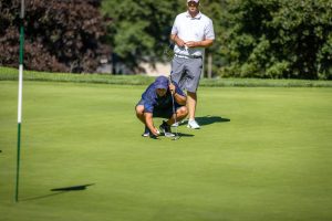 Golfer lining up putt while teammate watches