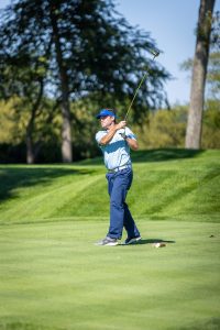 Golfer swinging club on sunlit green