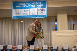 Two people holding award beneath sponsor banner